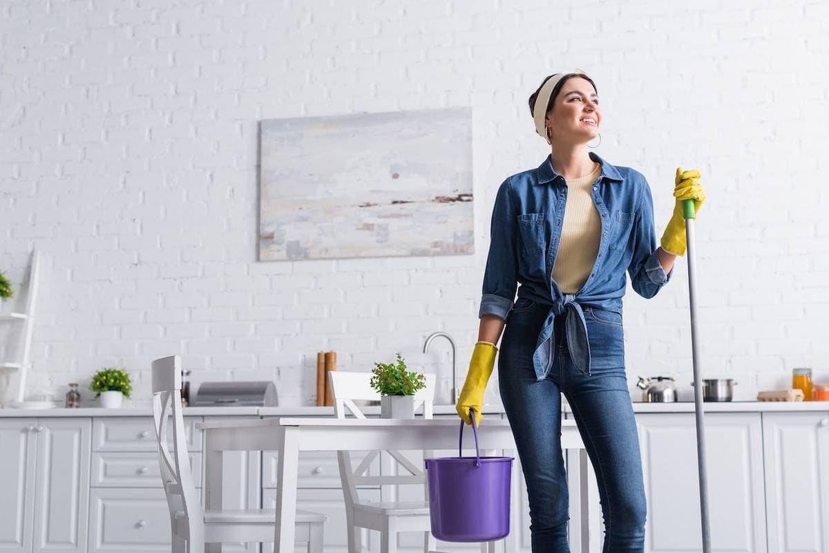 Cleaner mopping a kitchen floor beside a supplies bucket
